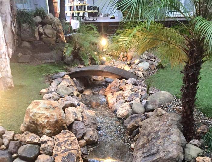 landscaping in Reseda, CA done by adding a small creek with natural rocks on sides and wooden bridge